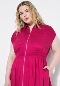 Abito fucsia con maniche corte a sbuffo, zip frontale e cintura elastica. Presenta due tasche sul petto e una gonna fluida.