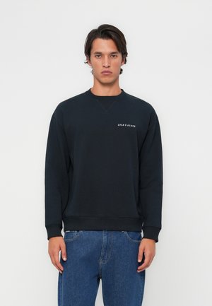 Black sweatshirt with crew neck, ribbed cuffs and hem, featuring a small white logo. Paired with light blue denim jeans.