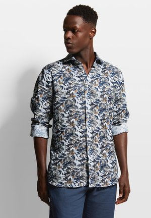 Long-sleeve shirt in white with blue, brown, and green floral pattern; button-down collar; rolled-up sleeves; lightweight fabric.