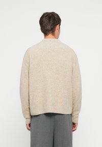 Beżowy, oversize sweter z miękkiego dzianiny z prążkowanym wykończeniem u dołu i na mankietach. Posiada okrągły dekolt i luźny krój.