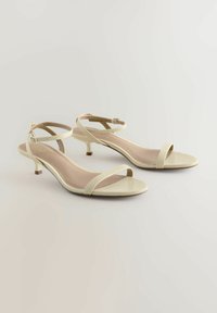 Beige sandaletter med remmar, med en texturerad vävd yta, låga kittenklackar och justerbara vristremmar, med en slät, ljus sula.