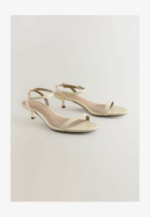 Beežid rihmad tossud tekstuurse kudumisega viimistluses, madalad kitten-kontsud ja reguleeritavad pahkluu rihmad, millel on sile, heledavärviline sisetald.