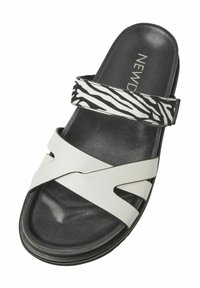 Weiße Rutschsandale mit einem gestreiften schwar-weißen Zebra-Musterriemen. Sie verfügt über eine weiche Textur, ein offenes Design und ein konturiertes Fußbett für Komfort.