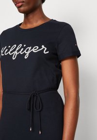 Granatowa sukienka T-shirt z białym logo "Hilfiger" w stylu sznurowania, krótkie rękawy i talia ze sznurkiem z metalowymi akcentami.