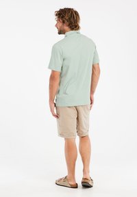 Lichtgroene polo met korte mouwen gecombineerd met beige shorts. Het shirt heeft een kraag en een subtiele textuur, terwijl de shorts knielang zijn.