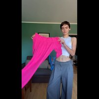 Felroze, elastisch shirt met een geraffineerde halslijn en lange mouwen, vastgehouden door een persoon in een witte cropped tanktop en grijze broek.