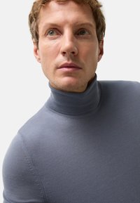 Pull en col roulé gris en tissu tricoté lisse, présentant une coupe ajustée et un léger côtelé au niveau du col et de l'ourlet.