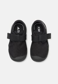 Zapatos negros con parte superior de malla y suela de goma, que presentan una correa ajustable a lo largo del empeine y detalles texturizados en los lados.