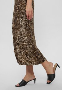 Vestido midi de leopardo con un diseño fluido. Combinado con sandalias de tacón bajo y abierto en la parte delantera, en color negro.