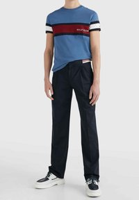 Camiseta de algodón azul con rayas horizontales en rojo, blanco y negro, combinada con pantalones de vestir azul marino con pliegues y zapatillas.