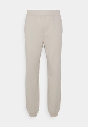 Pantalones jogger beige con cintura elástica, puños en los tobillos, detalles en las costuras delanteras y una textura de tela suave y lisa.