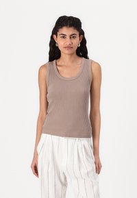 Beige ribbet tank topp med rund hals og horisontal tekstur, kombinert med hvite bukser med vertikale striper.