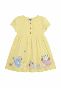 Keltainen pilkullinen mekko, joka on valmistettu puuvillasta, jossa on nappilista ja kirjailtuja hiiriä, kukkia ja puutarhaelementtejä helmassa.