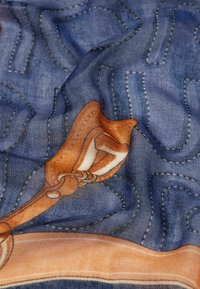 Bufanda de seda con una textura de denim azul y acentos gráficos en naranja y blanco, que incluyen líneas y formas estilizadas, drapeada y arrugada.