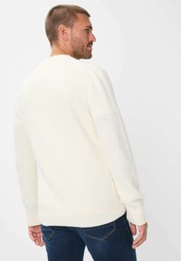 Maglione bianco lavorato a maglia con un motivo testurizzato; polsini e orlo a costine; indossato con jeans blu scuro, in mostra vista posteriore.