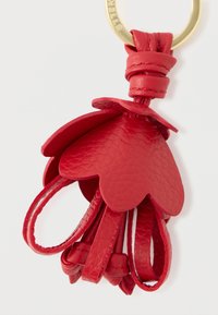 Czerwony skórzany brelok w kształcie płatków, z pętlą, teksturowaną powierzchnią i złotym uchwytem do kluczy.