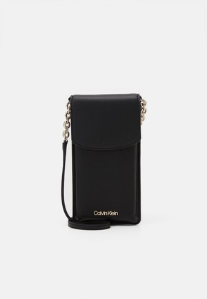 Bolso bandolera de cuero negro para teléfono con cierre de solapa, correa de cadena dorada y logo de Calvin Klein en la parte frontal.