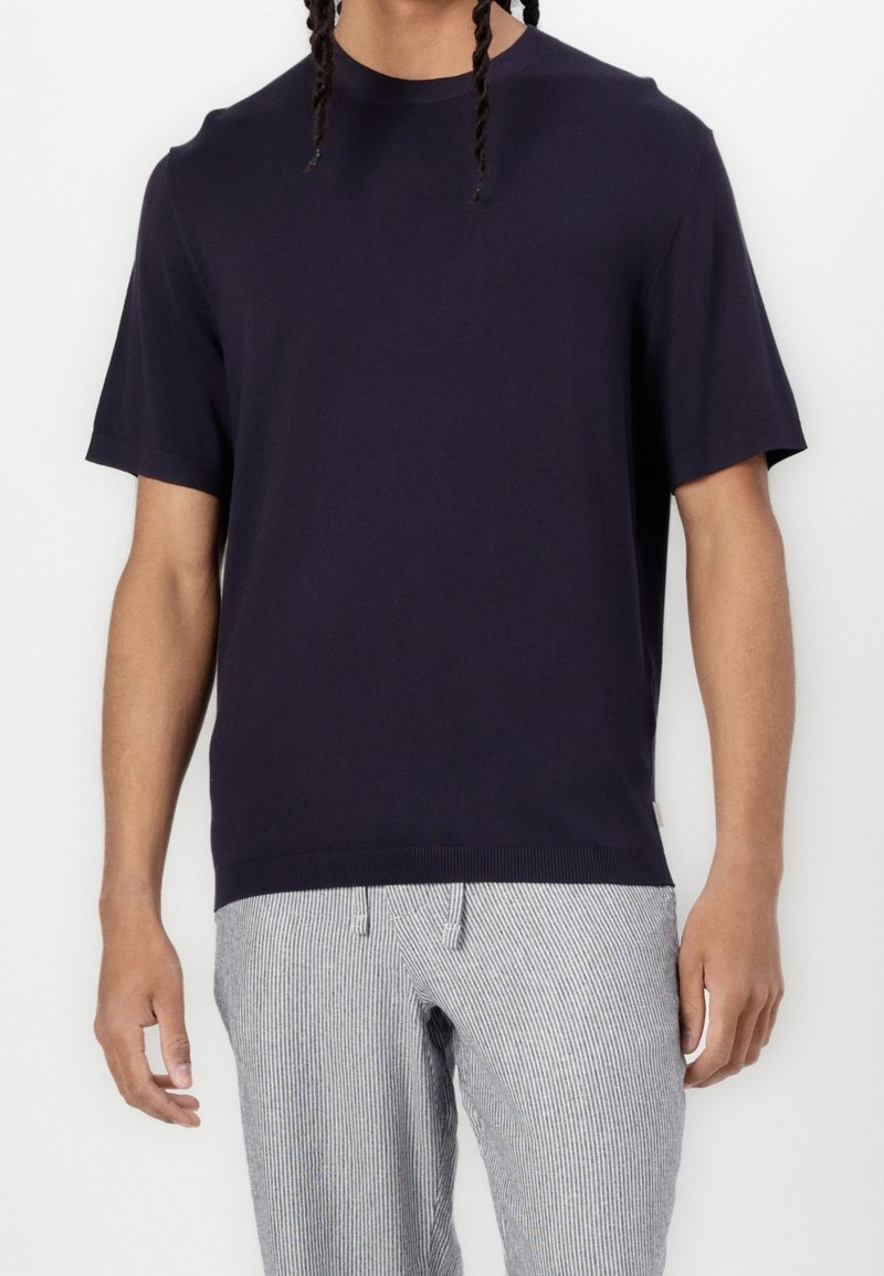 T-shirt bleu marine à manches courtes en coton doux, doté d'un col rond et de poignets côtelés, associé à un pantalon gris rayé.