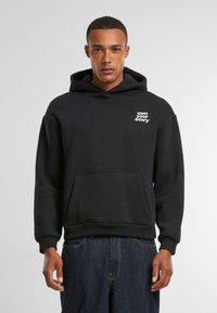 Schwarzer Kapuzenpullover aus weichem Stoff, mit einer Vordertasche und weißen Text "own your story" auf der linken Brust. Verstellbare Kordelzugkapuze.