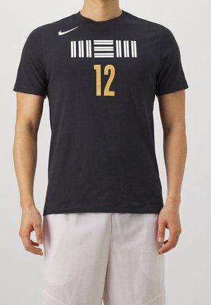 Osoba nosząca czarną koszulkę Nike z białym wzorem przypominającym kod kreskowy nad złotą cyfrą 12, w połączeniu z białymi siateczkowymi szortami.