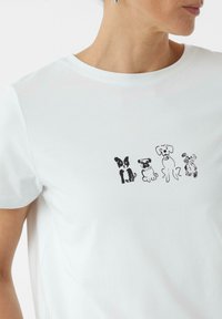 Witte katoenen t-shirt met een zwart grafisch illustratie van vier verschillende hondenrassen die in een rij op de voorkant zijn geplaatst.