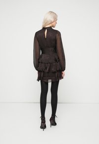 Μαύρο μίνι φόρεμα με στρώσεις και διαφανείς μακριές μανσέτες, διαθέτει δαντελωτό άνοιγμα στην πλάτη, εφαρμοστό στη μέση και ρουφάκια. Φοριέται με μαύρες καλτσόν και τακούνια.