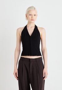 Black halter top with a deep V-neck and cropped design. Fabric appears smooth with minimal stitching. Worn with high-waisted brown trousers.