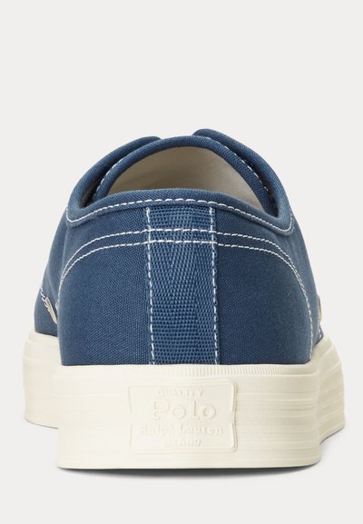Blå tygsneakers med vit gummisula, med kontrasterande vit söm och en texturerad bakpanel, med logotyp på hälen.