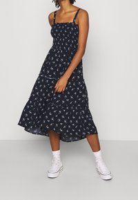 Blommig sommarklänning i marinblått, med ett stäppat mönster, justerbara band och små vita blommor. Matchad med vita sneakers.