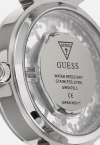 Rustfrit stål ur med en gennemsigtig bagside, der har et cirkulært kassedesign, klart glas og indgraveret mærke og specifikationer.