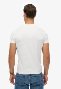 T-shirt bianco con maniche corte e collo rotondo, realizzato in tessuto di cotone, caratterizzato da una superficie liscia e un design aderente. Jeans in denim visibili.