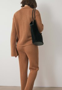 Pleteni rjav pulover in usklajene hlače z teksturiranim vzorcem, dopolnjeni z črno torbico z okroglo dno.