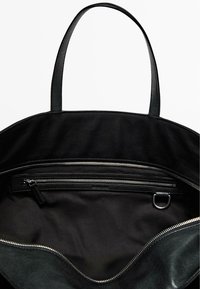 Zwarte tote bag met dubbele handvatten aan de bovenkant, voorzien van een ritscompartiment en een zachte stoffen binnenkant. Glad Textuur, ronde vorm.