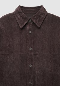 Camicia con bottoni in tessuto marrone scuro testurizzato. Presenta un colletto a punta e sei bottoni marroni, con due tasche sul petto delineate.