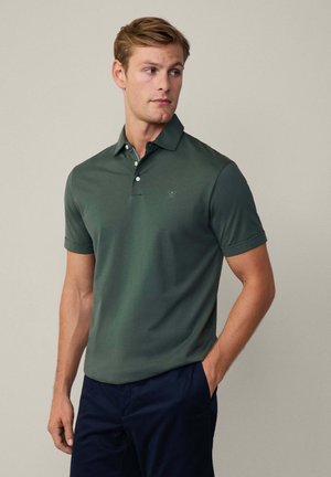 Polo-shirt vert foncé en tissu doux, à manches courtes et avec un col. Présente un petit logo sur la poitrine et une patte de boutonnage classique.