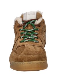 Bruine suede sneakers met groen en witte gemusterde veters, een gevoerde binnenkant en een leren rubberen zool. Het label leest "Certificaat van Oorsprong Sinds 2005."