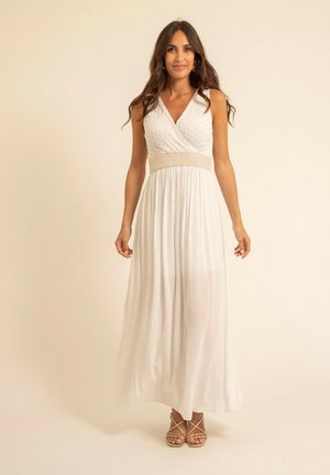 Robe maxi blanche avec un décolleté en V, un corsage texturé et une large ceinture beige texturée. Tissu léger et fluide avec des sandales à lanières.