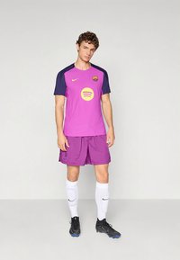 Lilla Nike jalgpallivarustus, mis sisaldab toonitoonis tekstuuri, lühikesi varrukasid, musti aktsente ja Spotify logo. Kandes sobivaid pükse ja musti saapaid.