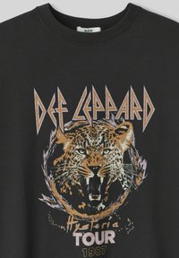T-shirt en coton noir avec un graphique de tigre rugissant en orange, accompagné du texte "DEF LEPPARD HYSTERIA TOUR 1987" en lettres métalliques.