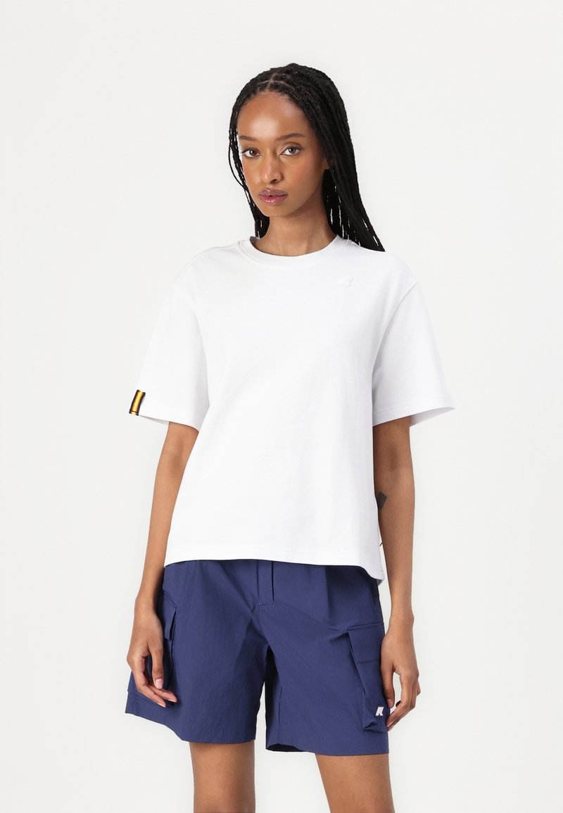 Tricou alb din bumbac cu mâneci scurte și guler rotund; prezintă un mic logo și un accent în dungi pe mâneca stângă; combinat cu pantaloni scurți bleumarin.