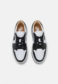 Pár černobílých Nike Air sneakers s černými šňůrkami, perforovanou špičkou a korkově texturovanými vnitřními podrážkami, viděný z vrchu na bílém pozadí.