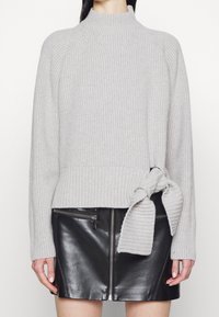 Ljusgrå stickad tröja med mockneck, ribbad struktur och detalj med sidoband. Kombinerad med en svart läderkjol med dragkedja.