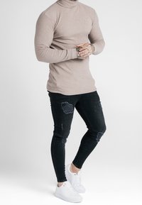 Maglione a collo alto rigato beige abbinato a jeans skinny neri strappati e sneakers bianche. Tra le caratteristiche troviamo un tessuto testurizzato e una vestibilità aderente.