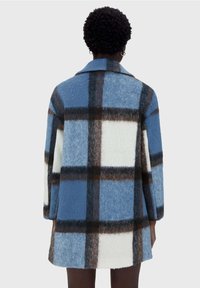 Abrigo de lana de cuadros azul y blanco con acentos en marrón, que presenta un cuello y mangas largas, mostrando una textura suave y un corte oversize.