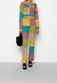 Ensemble à deux pièces à rayures colorées avec un hoodie court et un pantalon évasé, présentant un design en patchwork dans des tons de vert, jaune, bleu et rose.