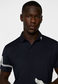 Navy polo shirt with a two-button placket, short sleeves, and a striped pattern on the left sleeve. Features distinctive logo on the collar.