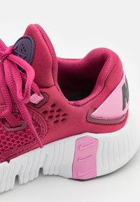 Pink atletiksko med en meshlæg og teksturerede detaljer, runde snørebånd og en hvid gummisål med pink detaljer og logo.