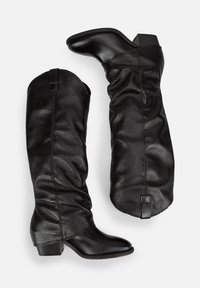 Botas negras hasta la rodilla con parte superior de cuero perforado, diseño arrugado y un tacón bajo. Incluyen tiradores en la parte superior para facilitar el uso.