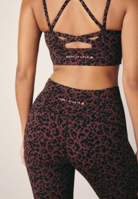 Soutien-gorge de sport et leggings à imprimé léopard en rouge foncé et noir. Comprend des bretelles croisées et une marque discrète à la taille.