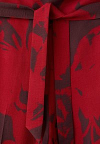 Tissu rouge à motif floral foncé noué en nœud ou en boucle, montrant la texture et les plis du matériau.